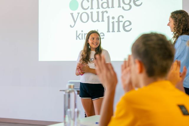Una chica presenta ante una pantalla con el logo del Change Your Life Kindle